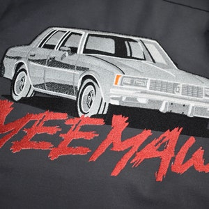 Puede incluir: Un coche vintage gris con la palabra "MEEMAW" bordada en rojo sobre un fondo gris oscuro.