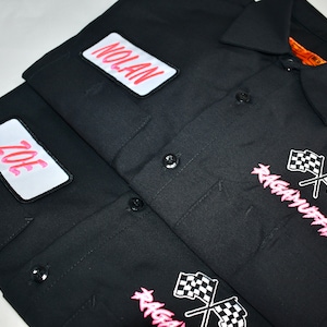May include: Black work shirt with two pink patches that say "Joe" and "Nolan". The shirt has a pink and white checkered flag graphic with the text "Raggamuffin" in pink.