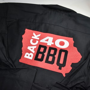 May include: Black work shirt with a red patch featuring the text "Back 40 BBQ" in white and black lettering, shaped like the state of Iowa.