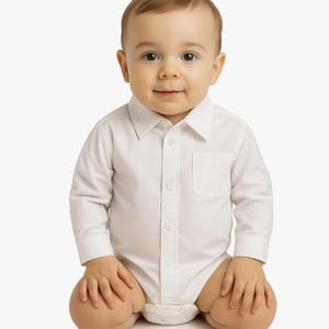 May include: A crisp white long-sleeved button-down bodysuit featuring a classic pointed collar, a single chest pocket, and a front button placket. The garment is designed with a structured shirt-style top that transitions into a snap-closure bottom.