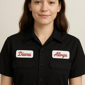 May include: Black short-sleeved work shirt with two chest pockets and a button-down front. The shirt has two patches, one with the name "Diana" and the other with the name "Alvys", both in red script on a white background.
