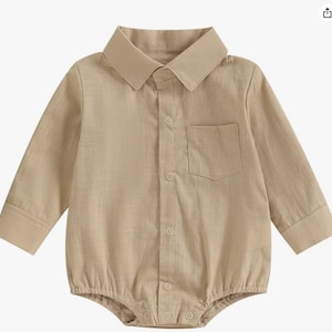 May include: A long-sleeved beige button-down romper featuring a classic collar, a single chest pocket, and a buttoned placket down the front. The garment has a structured collar and cuffs, with a snap-button closure at the bottom hem area.