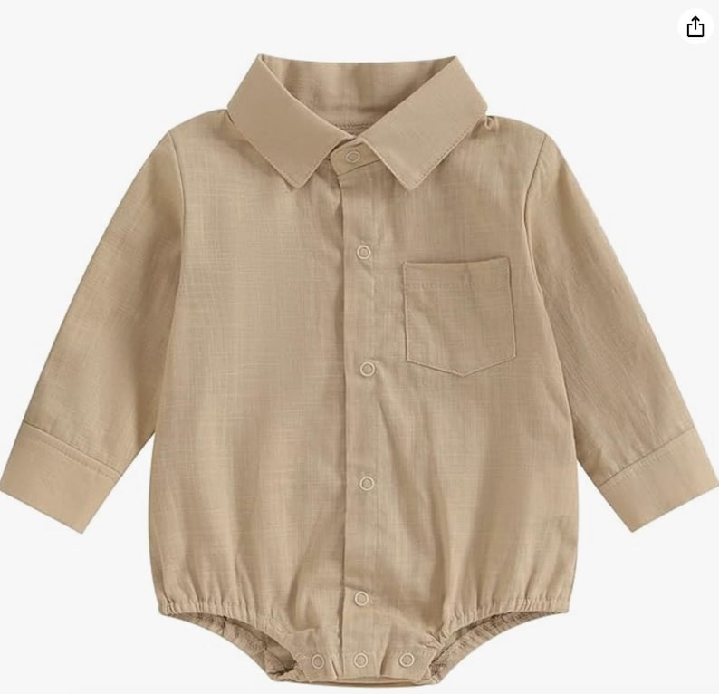 May include: A long-sleeved beige button-down romper featuring a classic collar, a single chest pocket, and a buttoned placket down the front. The garment has a structured collar and cuffs, with a snap-button closure at the bottom hem area.