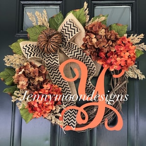 May include: A fall-themed wreath with a large orange letter Y, a burlap bow with black and white chevron ribbon, and orange and brown hydrangea flowers.