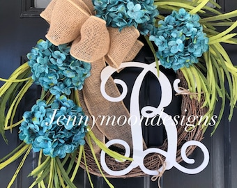 May include: A teal and green wreath with a burlap bow and a white wooden letter R in the center. The wreath is made of grapevine and has a rustic look. The text "Jennymoon Designs" is visible in the bottom left corner of the image.