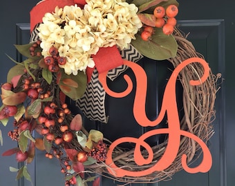 May include: A fall-themed wreath with a burlap bow, orange berries, and a large orange letter "Y" on a brown vine base.