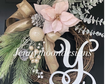 May include: A Christmas wreath with a pink poinsettia, gold and brown ribbon, and a white wooden letter Y. The wreath is decorated with pine branches, white berries, and a gold ornament. The text "Jennymoondesigns" is visible on the wreath.