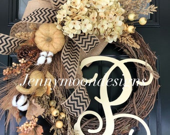 May include: A fall-themed wreath with a burlap bow, white hydrangeas, gourds, cotton bolls, and a large white wooden letter "P".