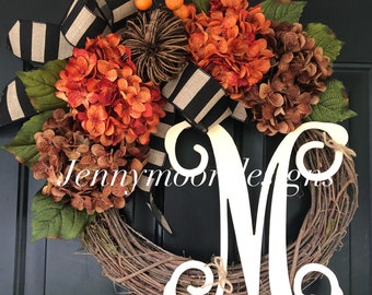 May include: A fall-themed wreath with orange and brown hydrangeas, black and white striped ribbon, and a large white wooden letter "M".