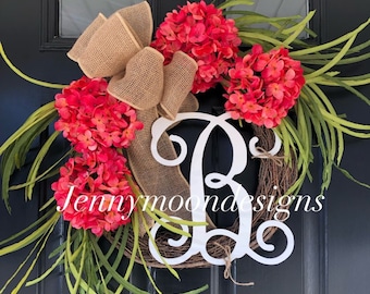 May include: A wreath with a burlap bow, pink flowers, and green leaves. The wreath has a white wooden letter "R" in the center. The text "jennymoondesigns" is visible at the bottom of the wreath.