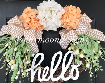 May include: A peach, white, and green floral wreath with a burlap bow and the word "hello" in white lettering.