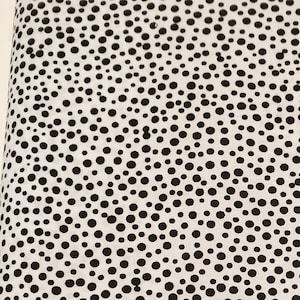 May include: White fabric with a black polka dot pattern. The dots are of varying sizes and are randomly distributed.