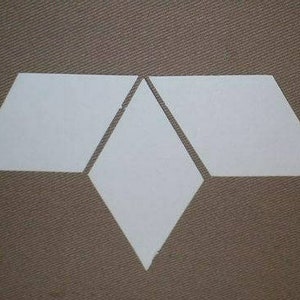 May include: Four white geometric shapes arranged on a brown textured surface. The shapes include two trapezoids, a diamond, and a trapezoid. The shapes are arranged to form a stylized design.