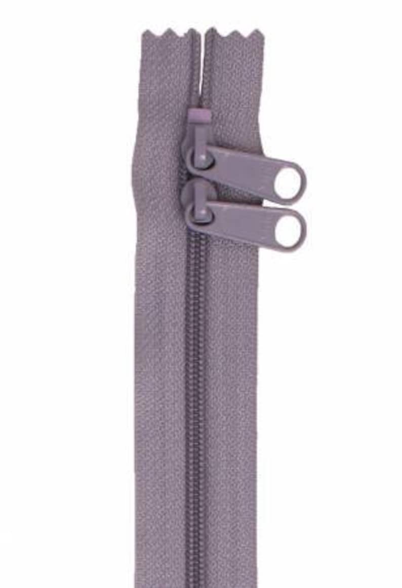 May include: A gray zipper with two metal sliders. The zipper is closed and ready to be sewn into a garment.