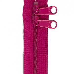 May include: A pink zipper with two pull tabs. The zipper is closed and the pull tabs are in the up position.