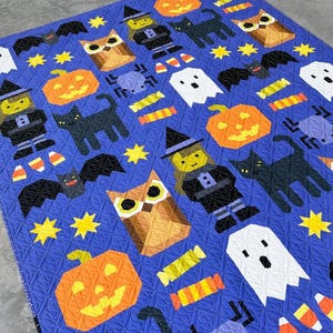 May include: A blue Halloween-themed quilt featuring repeating patterns of orange pumpkins, black cats, bats, owls, ghosts, witch figures, spiders, candy corn, and yellow stars. The quilt is machine-stitched with a quilted texture.