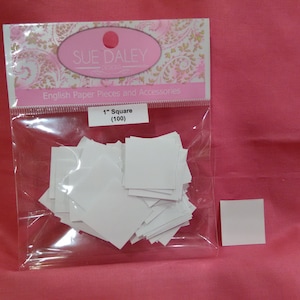 May include: A clear plastic bag containing 100 white 1-inch square paper pieces. The bag has a label that reads "Sue Daley Designs" and "English Paper Pieces and Accessories". The label also says "1" Square (100)".