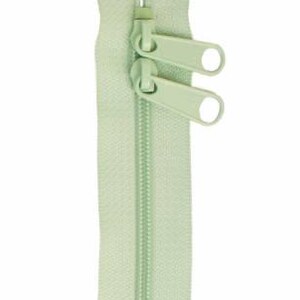 May include: A light green zipper with two pull tabs. The zipper is closed and ready to be sewn into a garment.