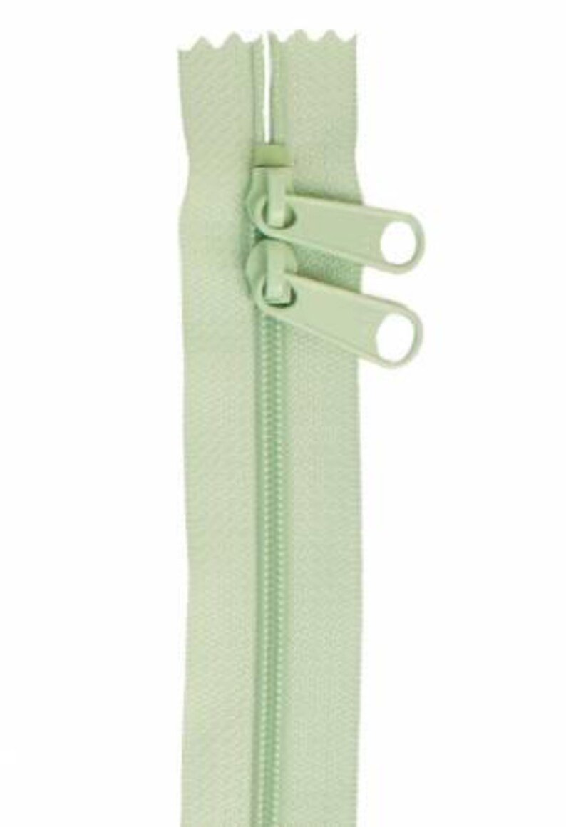 May include: A light green zipper with two pull tabs. The zipper is closed and ready to be sewn into a garment.