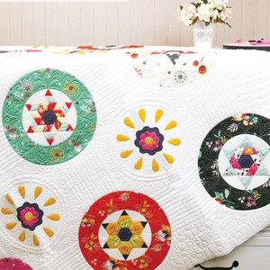 May include: A white quilt with a variety of colorful circles. The circles feature different patterns, including floral, geometric, and star-shaped designs. The quilt is quilted with a decorative stitch.