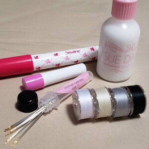 May include: A set of sewing supplies including a bottle of Sue Daley Fabric Glue, a pink Sewline marker, a small tube of milliners needles size 11, a spool of white thread, a spool of cream thread, a spool of gray thread, and a spool of black thread.