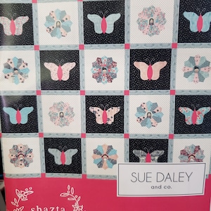 May include: A quilt pattern featuring a butterfly design with a pink butterfly on a black background. The pattern is called "Butterfly Love" and is by Sue Daley and Co. The pattern is from Shazcta Daisy, est. 2014.