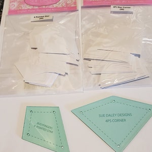 May include: Two packages of white paper pieces for quilting, one labeled "4 Pointed Star (50)" and the other labeled "4Pt Star Corner (50)". Two clear plastic templates for quilting, one labeled "Busyfingers 4 Pointed Star" and the other labeled "Sue Daley Designs 4Ps Corner".
