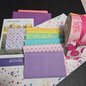 May include: A collection of quilting supplies, including fabric bundles in various colors and patterns, a jelly roll, and two quilting pattern books. The fabrics feature geometric and floral designs in shades of pink, purple, blue, and yellow. A pink ribbon secures the jelly roll.