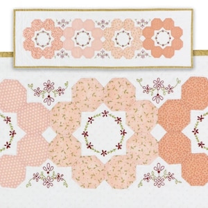 May include: A floral quilt in shades of peach and white. The quilt features a repeating pattern of octagonal shapes and large flower designs. The flowers have embroidered centers and are surrounded by a wreath of small flowers. The quilt is bordered with a gold trim.