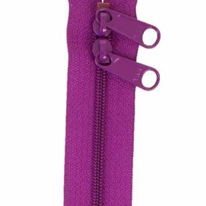 May include: A purple zipper with two metal sliders. The zipper is closed and ready to be sewn into a garment.