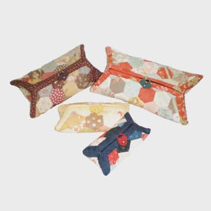 May include: Four handmade fabric pouches in various sizes and colors. The pouches feature a patchwork design with hexagonal fabric pieces in shades of red, brown, blue, and yellow. Each pouch has a button closure.
