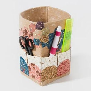 May include: A beige fabric organizer with a patchwork design. The organizer holds black scissors, a pink and white marker, and a yellow ruler. The patchwork features floral and geometric patterns in shades of blue, pink, and brown.
