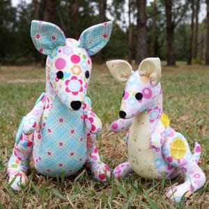 May include: Two handmade plush kangaroo toys. The larger kangaroo is blue, pink, and white with a floral pattern. The smaller kangaroo is yellow, pink, and white with a floral pattern.