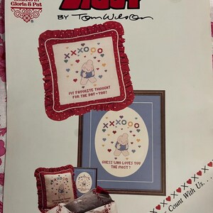 May include: A vintage "Ziggy" cross-stitch pattern by Tom Wilson. The design features a cartoon bear with the text "My Favorite Thought For The Day - You!" and "Guess Who Loves You The Most?" in a framed image. The pattern includes hearts and XOXO symbols.