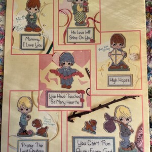 May include: A cross-stitch pattern booklet featuring six distinct designs of children with inspirational text including Mommy I Love You, His Love Will Shine On You, High Hopes, You Have Touched So Many Hearts, Praise The Lord Anyhow, and You Can't Run Away From God.