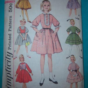 May include: Vintage Simplicity sewing pattern for a 7-day wardrobe dress. The pattern includes instructions and diagrams for making a variety of dresses, including a gingham dress, a red dress, and a pink dress. The pattern is for size 10 and is printed on a white background with black text.