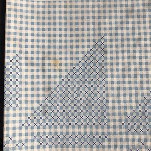 May include: A book cover with the title "Cross-Stitching and beauty to" printed in blue text. The background is a blue and white gingham pattern with a blue cross-stitch design in the center.
