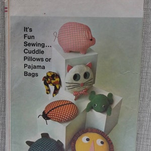 May include: Simplicity sewing pattern 7367 for cuddle pillows or pajama bags. The image shows various stuffed animal designs, including a pig, cat, ladybug, frog, turtle, and lion. The pattern is one size.