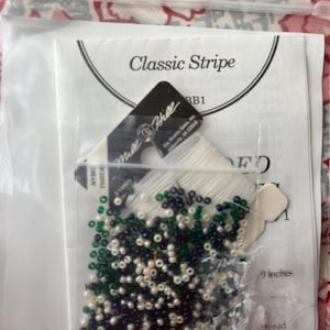May include: A craft kit in a clear plastic bag. The kit includes white thread, small beads in white, navy, and green, and a paper insert that reads "Classic Stripe". The kit is 9 inches in length.