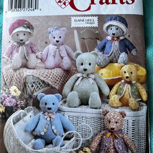 May include: A Simplicity Crafts pattern featuring various teddy bears in different outfits. The bears are in a variety of colors, including pink, blue, and yellow, and are displayed on a white wicker basket and a white wicker baby carriage.