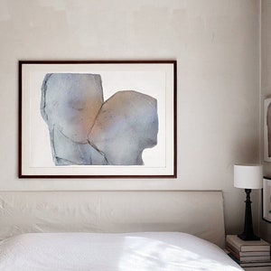 A bedroom wall decor with a dark wood framed high quality art print of a romantic abstract portrait of a love couple kiss in greige, dovetail and silver grey on white. The torn paper have grungy edges and a mural feel. The kiss glows opaque gold.