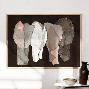 May include: Abstract art print featuring a collage of torn paper shapes in shades of white, gray, and beige against a dark brown background. The artwork is framed in a light wood frame, creating a minimalist aesthetic.