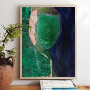 May include: Abstract painting in a wooden frame with a green, blue, and pink color scheme. The painting is hanging on a white wall above a stack of books.