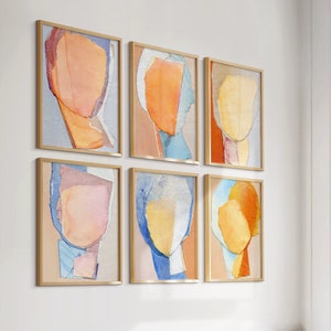 May include: Six abstract art prints in gold frames, each featuring a different color combination of pink, blue, yellow, and orange. The prints are arranged in a grid pattern on a white wall.