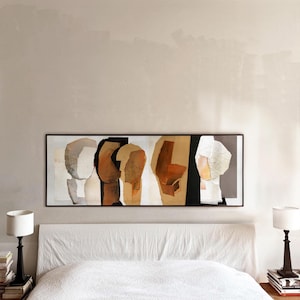 May include: A long rectangular framed wall art piece featuring abstract shapes in shades of brown, black, white, and beige. The artwork displays a series of geometric and organic forms arranged horizontally within a thin dark frame on a wall.