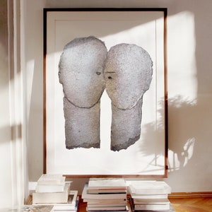 A decor with dark wood framed high quality art print of a romantic abstract portrait. It is a love couple in shades of grey with silver finish on white. The heads are composed of torn rough paper layers, exposed grungy edges and two eyes for accent.