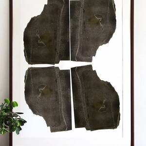 A wall decor with a monochromatic large statement art print of an abstract original portrait with four heads in shades of brushed oil black on a shiny wooden table and some flowers. It has parallel straight torn paper layers for a geometrical feel.