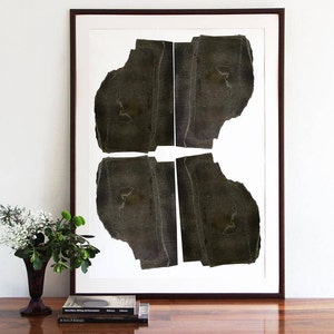 A wall decor with a monochromatic large statement art print of an abstract original portrait with four heads in shades of brushed oil black on a shiny wooden table and some flowers. It has parallel straight torn paper layers for a geometrical feel.