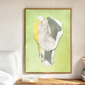 May include: Abstract art print in a gold frame. The artwork features torn paper collage elements in shades of yellow, grey, and white against a light green background. The framed art is displayed on a wooden nightstand.
