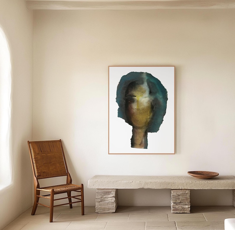May include: A framed abstract painting of a face with a teal and yellow color scheme. The painting is hanging on a white wall above a concrete bench.